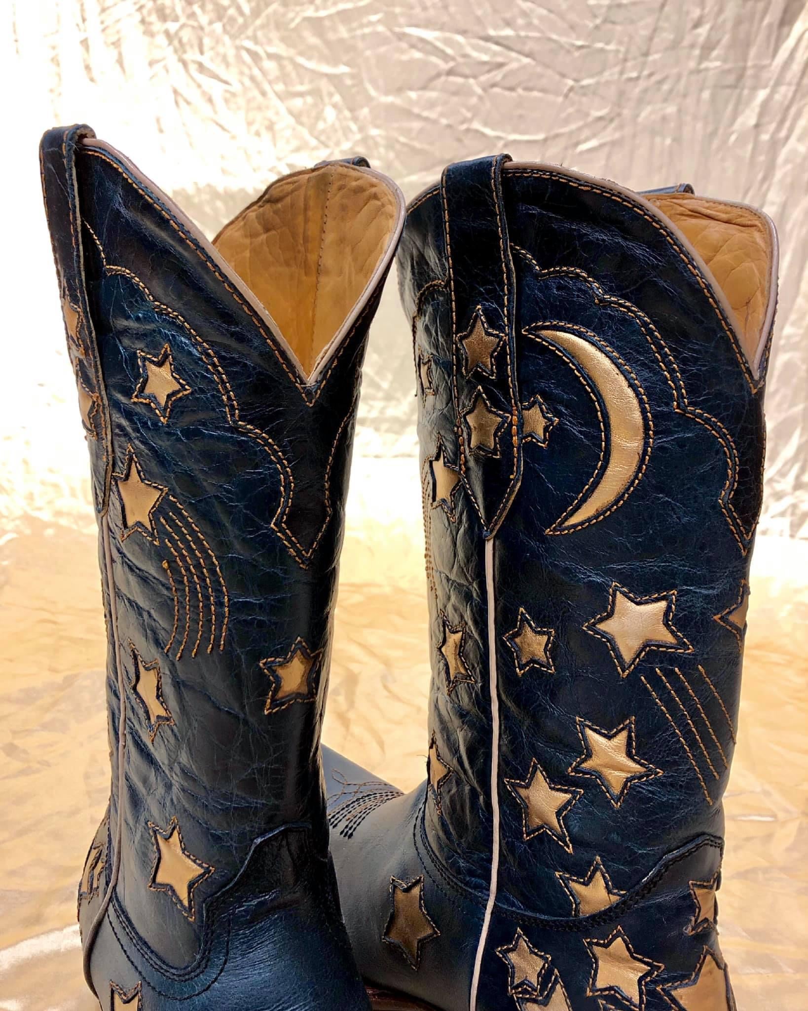 A pair of navy blue custom cowboy boots with a custom embroidery design of shooting stars and a half moon