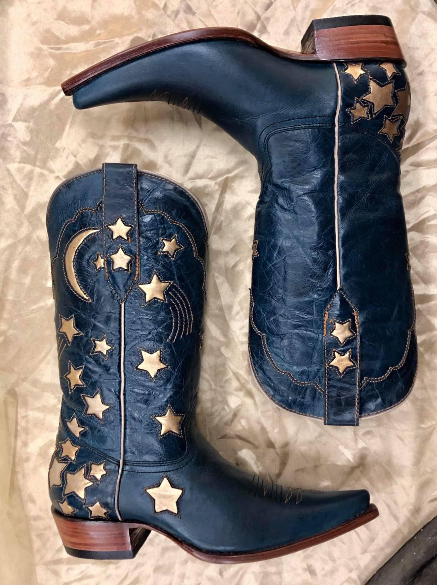 A pair of navy blue custom cowboy boots with a custom embroidery design of shooting stars and a half moon